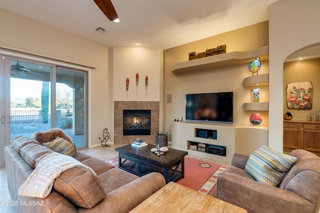 living area featuring baseboards, ceiling fan, visible vents, and a tiled fireplace