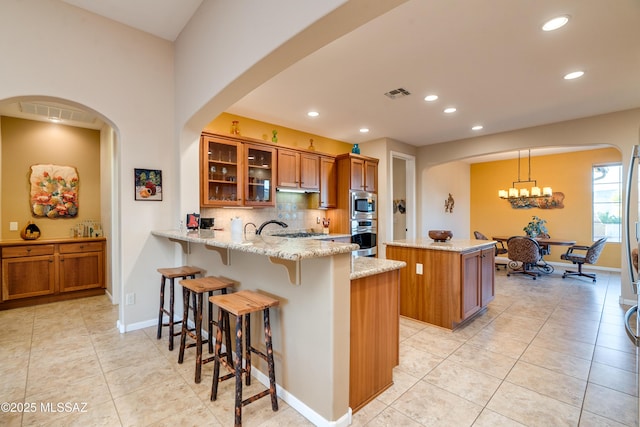 kitchen featuring brown cabinets, tasteful backsplash, visible vents, a kitchen island, and a peninsula