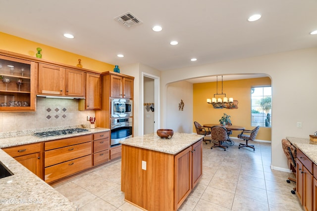 kitchen featuring arched walkways, stainless steel appliances, visible vents, brown cabinets, and tasteful backsplash