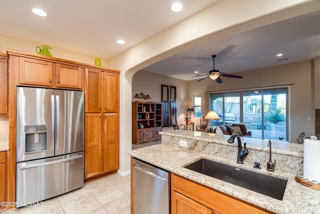 kitchen with arched walkways, appliances with stainless steel finishes, a sink, and light stone countertops