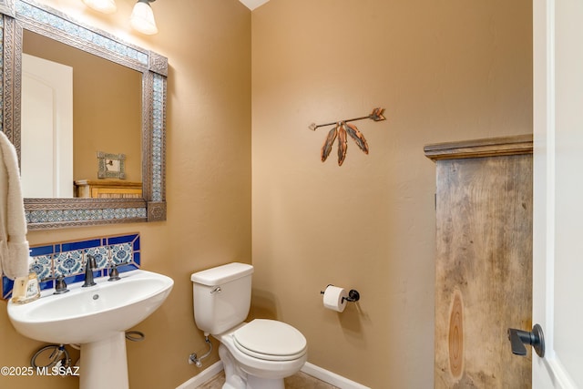 half bath with tasteful backsplash, baseboards, and toilet