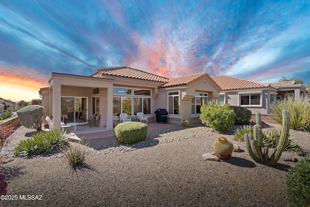 back of house at dusk featuring a tiled roof, a patio area, and stucco siding