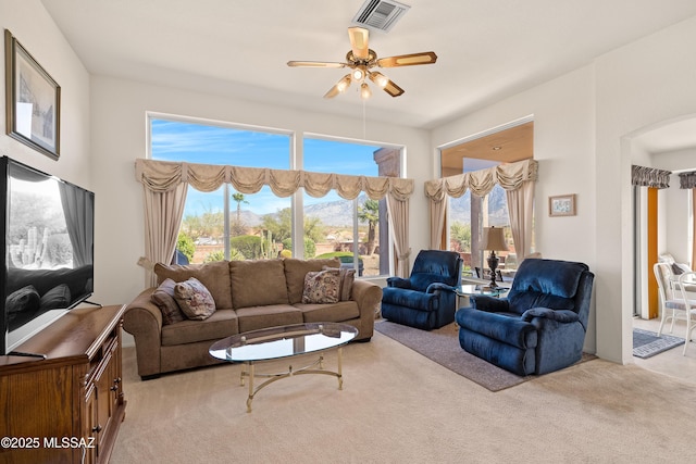 living area with light colored carpet, visible vents, ceiling fan, and arched walkways