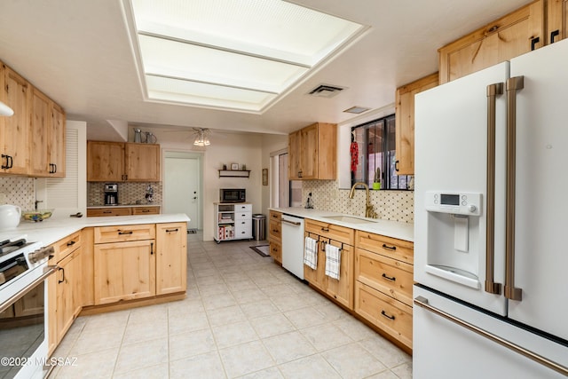 kitchen featuring light brown cabinets, light countertops, white appliances, and a sink