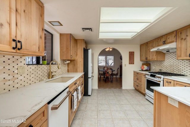 kitchen featuring arched walkways, under cabinet range hood, white appliances, a sink, and visible vents