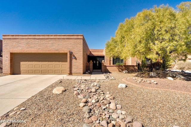 pueblo-style home with driveway, a garage, and brick siding