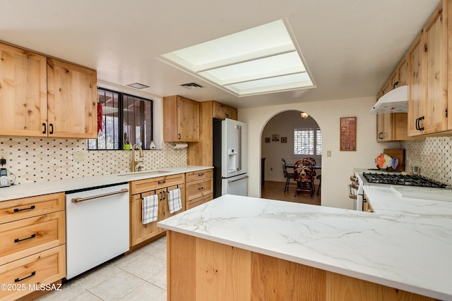 kitchen with white appliances, arched walkways, decorative backsplash, a peninsula, and under cabinet range hood