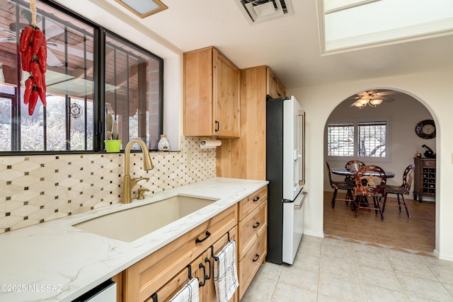 kitchen with light tile patterned floors, white refrigerator with ice dispenser, visible vents, arched walkways, and decorative backsplash