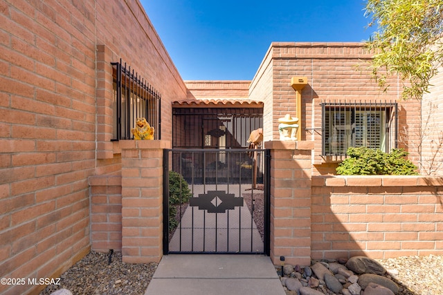 property entrance with a tile roof, a gate, brick siding, and fence