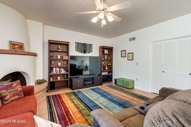 tiled living area featuring visible vents, ceiling fan, and a fireplace with raised hearth