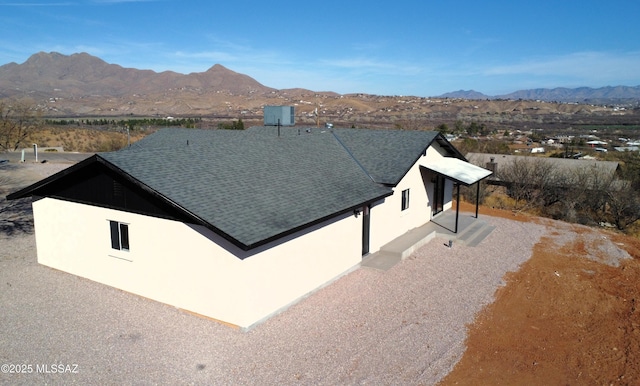 exterior space featuring stucco siding, a mountain view, and roof with shingles