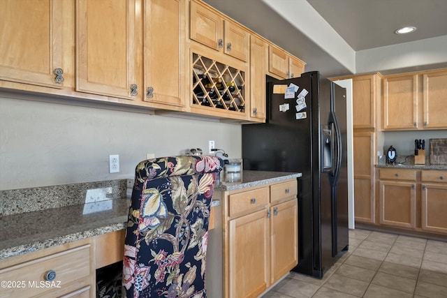 kitchen featuring light tile patterned floors, light stone counters, black refrigerator with ice dispenser, and light brown cabinetry