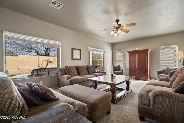 living room featuring a ceiling fan, visible vents, and light colored carpet