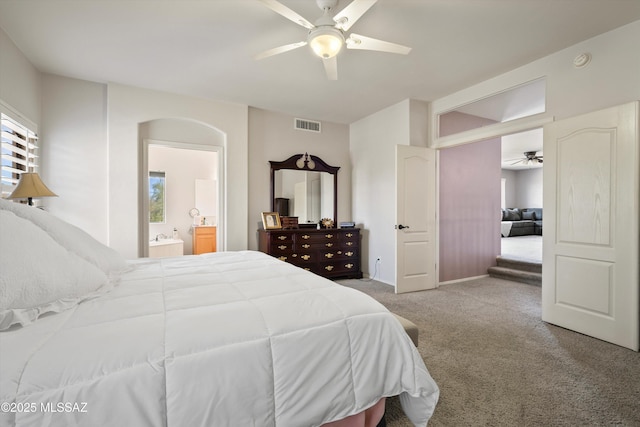 carpeted bedroom featuring a ceiling fan, arched walkways, visible vents, and ensuite bathroom