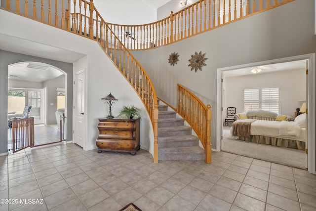 stairway featuring arched walkways, a towering ceiling, and tile patterned floors