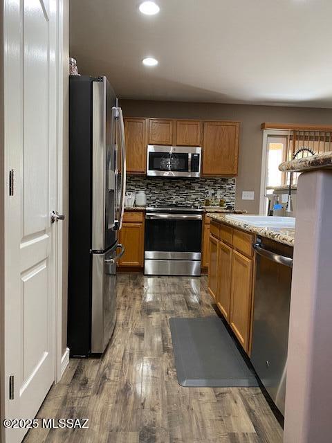 kitchen featuring stainless steel appliances, tasteful backsplash, dark wood-style flooring, and brown cabinets