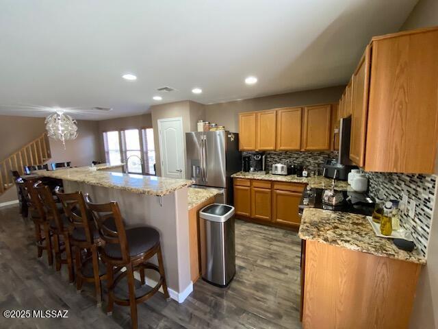 kitchen featuring dark wood-style floors, appliances with stainless steel finishes, a center island with sink, and tasteful backsplash