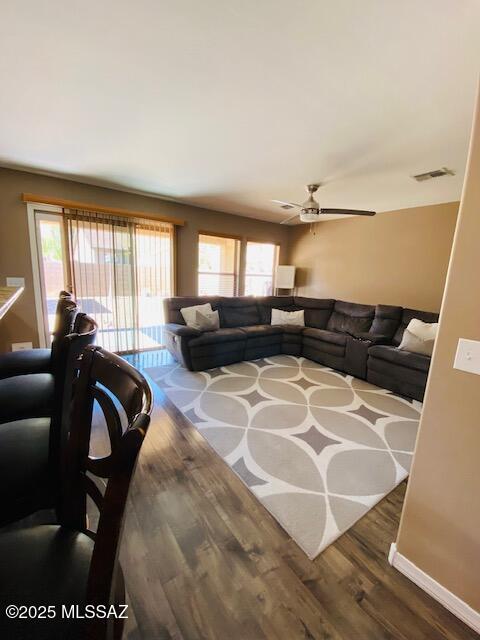 living room with ceiling fan, wood finished floors, visible vents, and baseboards