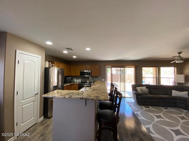 kitchen with visible vents, a kitchen breakfast bar, dark wood-style flooring, a peninsula, and stainless steel appliances