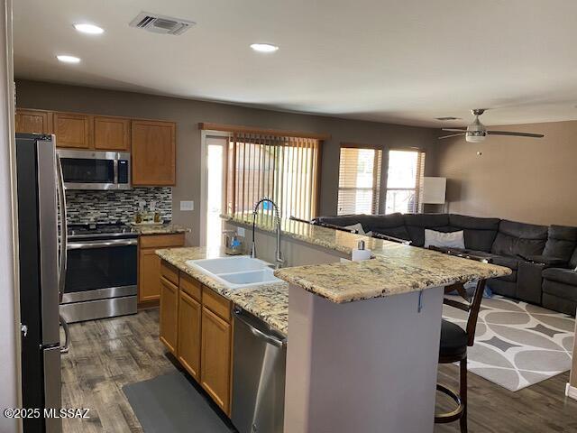 kitchen featuring visible vents, appliances with stainless steel finishes, open floor plan, dark wood-type flooring, and a sink