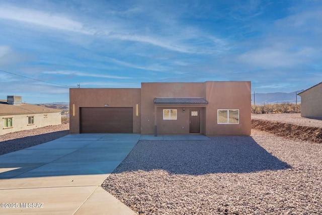 pueblo-style house featuring an attached garage, a mountain view, a tile roof, driveway, and stucco siding