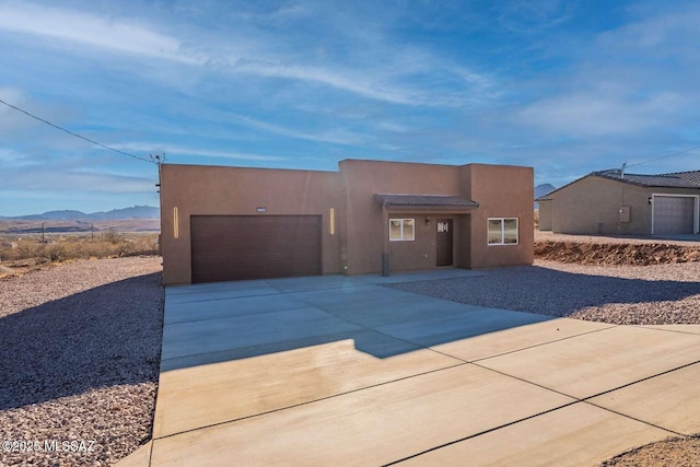 pueblo-style house featuring concrete driveway, a mountain view, an attached garage, and stucco siding