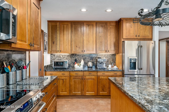 kitchen with decorative backsplash, appliances with stainless steel finishes, brown cabinets, and dark stone countertops