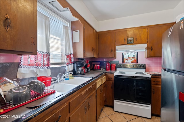 kitchen featuring electric range oven, brown cabinets, freestanding refrigerator, under cabinet range hood, and a sink