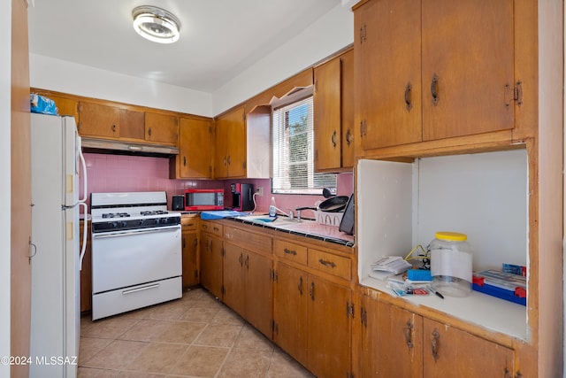 kitchen with white appliances, tasteful backsplash, brown cabinets, under cabinet range hood, and a sink