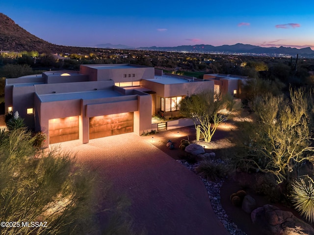 pueblo-style house featuring a mountain view, an attached garage, driveway, and stucco siding