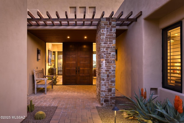 view of exterior entry featuring a pergola and stucco siding