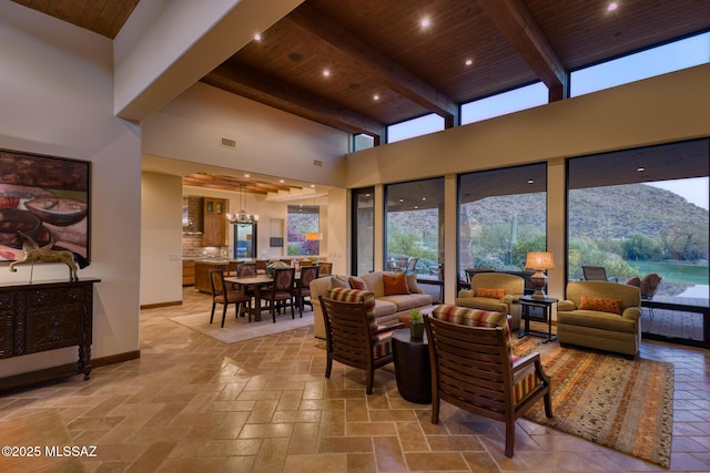 living area with visible vents, beamed ceiling, a high ceiling, wooden ceiling, and baseboards