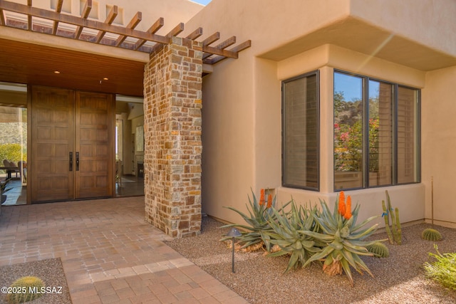 view of exterior entry featuring stucco siding and a pergola