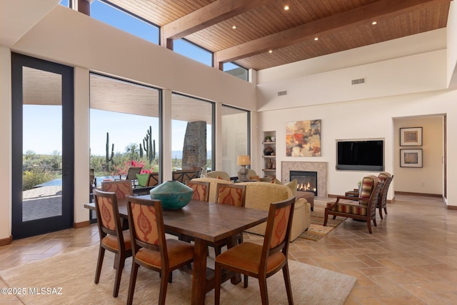 dining room with beamed ceiling, stone tile flooring, a lit fireplace, wood ceiling, and a towering ceiling