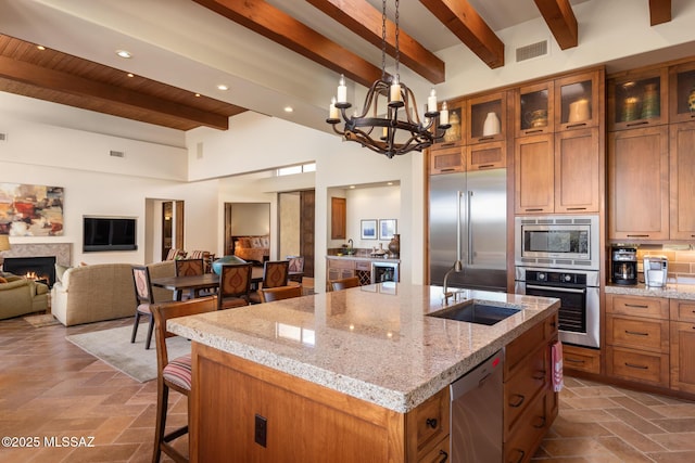 kitchen with stone tile floors, an island with sink, built in appliances, and a warm lit fireplace