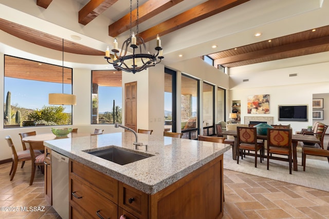 kitchen with a kitchen island with sink, stone tile flooring, a sink, stainless steel dishwasher, and open floor plan