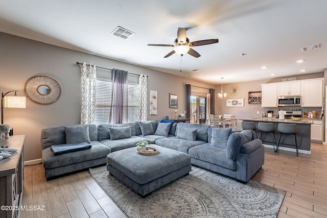 living area with visible vents, light wood-style flooring, baseboards, and ceiling fan with notable chandelier