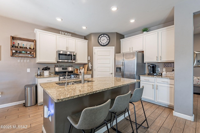 kitchen with appliances with stainless steel finishes, wood tiled floor, white cabinets, and an island with sink