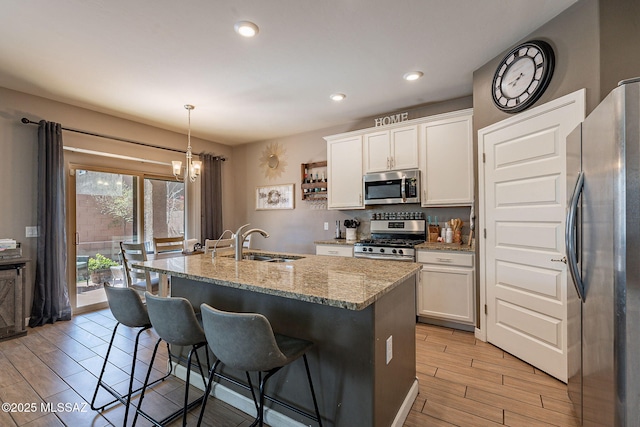 kitchen featuring decorative light fixtures, a sink, white cabinets, appliances with stainless steel finishes, and a center island with sink