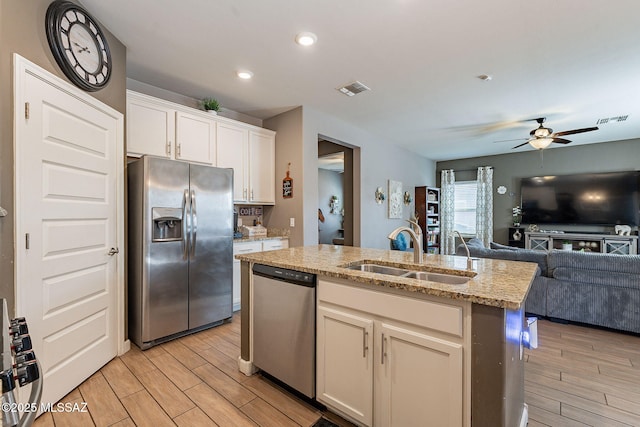 kitchen featuring appliances with stainless steel finishes, open floor plan, white cabinetry, a sink, and an island with sink