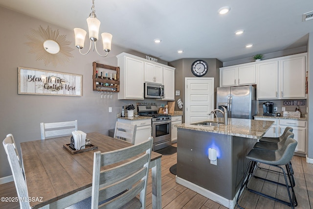 kitchen featuring appliances with stainless steel finishes, white cabinets, a center island with sink, and a sink