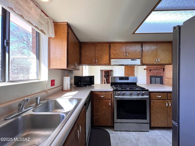 kitchen featuring under cabinet range hood, a sink, light countertops, appliances with stainless steel finishes, and brown cabinetry