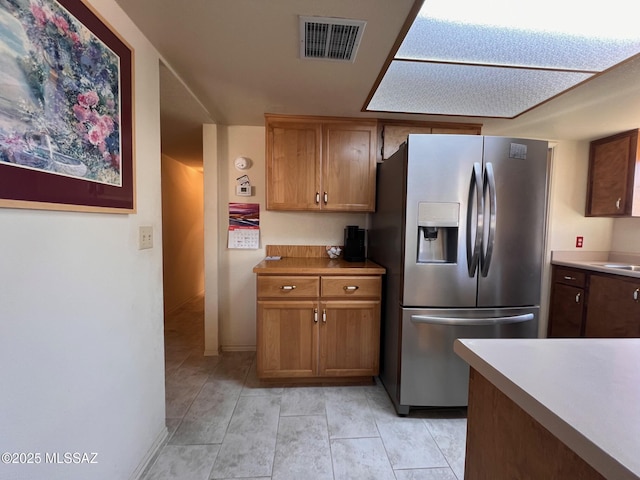 kitchen with brown cabinetry, visible vents, stainless steel refrigerator with ice dispenser, and light countertops