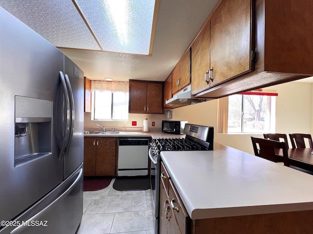 kitchen featuring a textured ceiling, light tile patterned flooring, a sink, light countertops, and appliances with stainless steel finishes