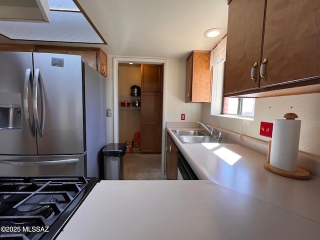 kitchen featuring cooktop, stainless steel fridge, dishwasher, light countertops, and a sink