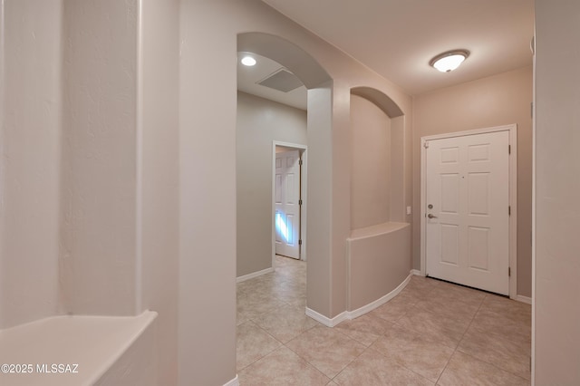 hall featuring arched walkways, light tile patterned floors, and baseboards