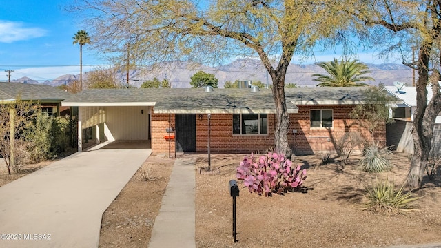 single story home with a mountain view, brick siding, concrete driveway, roof with shingles, and a carport