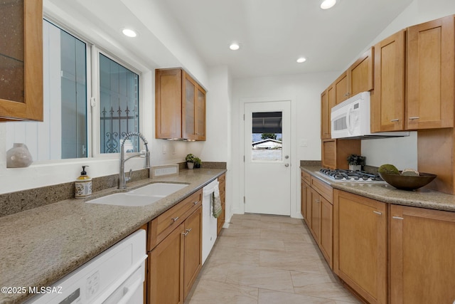 kitchen with white appliances, glass insert cabinets, light stone counters, and a sink