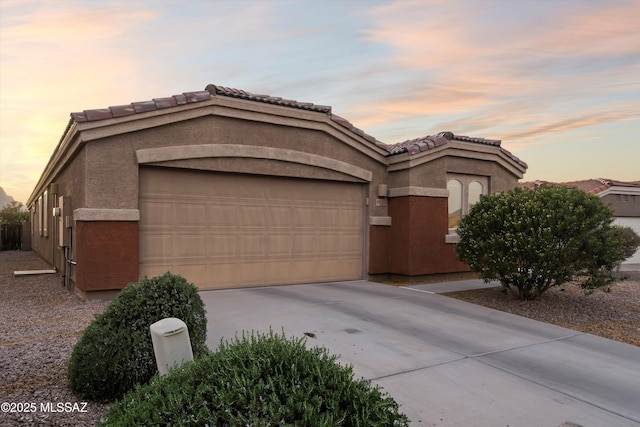 mediterranean / spanish home featuring driveway, a tile roof, a garage, and stucco siding