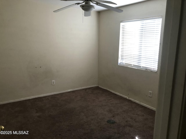 spare room with dark colored carpet, ceiling fan, and baseboards